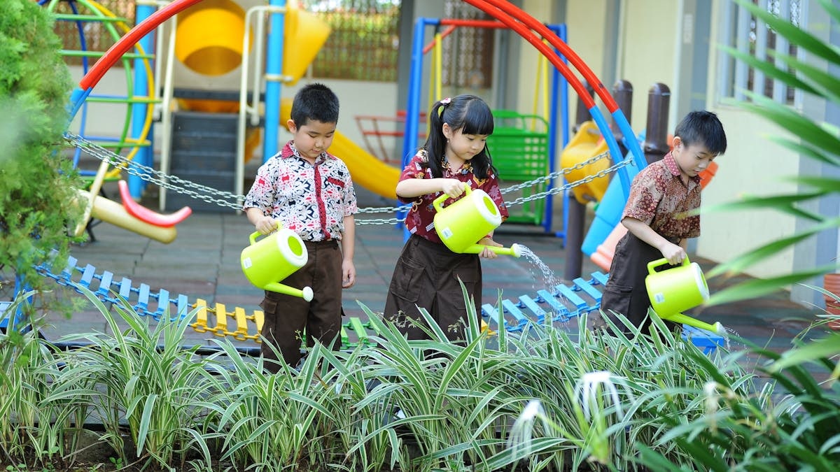 Young kids learning gardening skills by watering plants in a vibrant school playground setting.